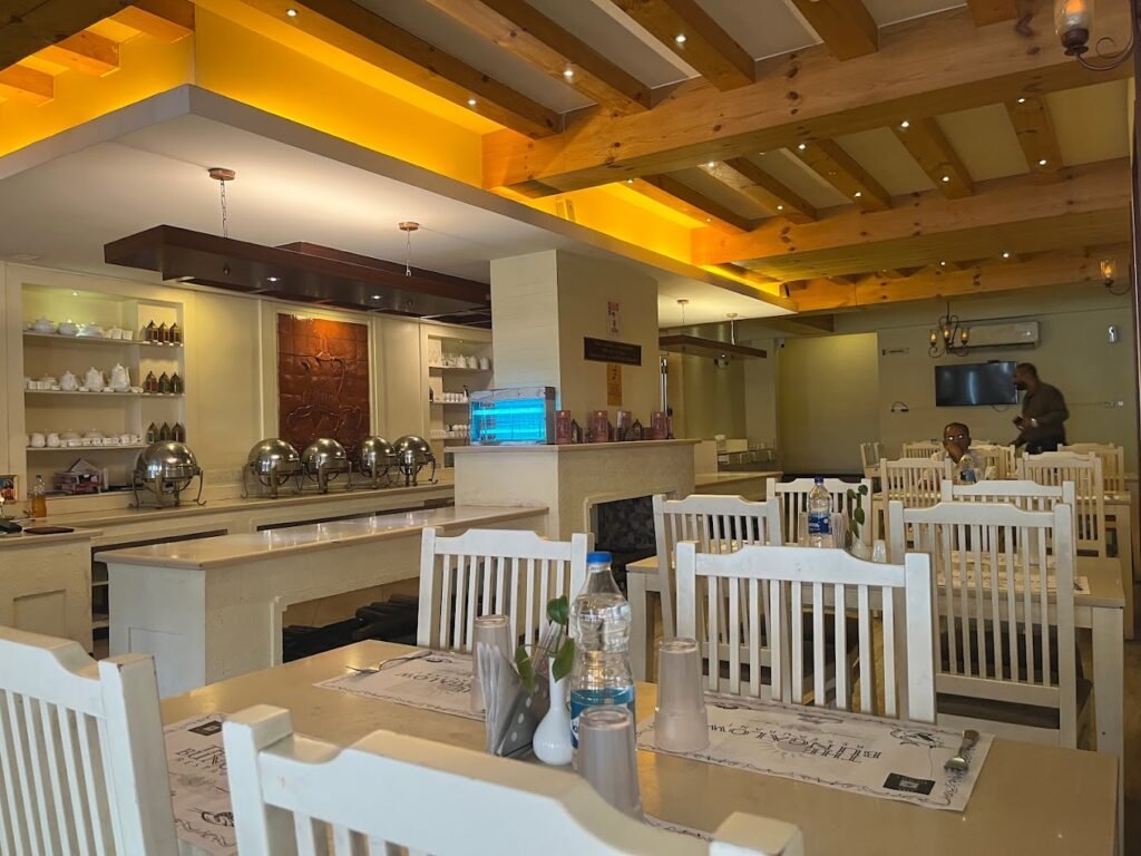 The interior of Bungalow  restaurant in Wayanad with white chairs , table and a dim lighting